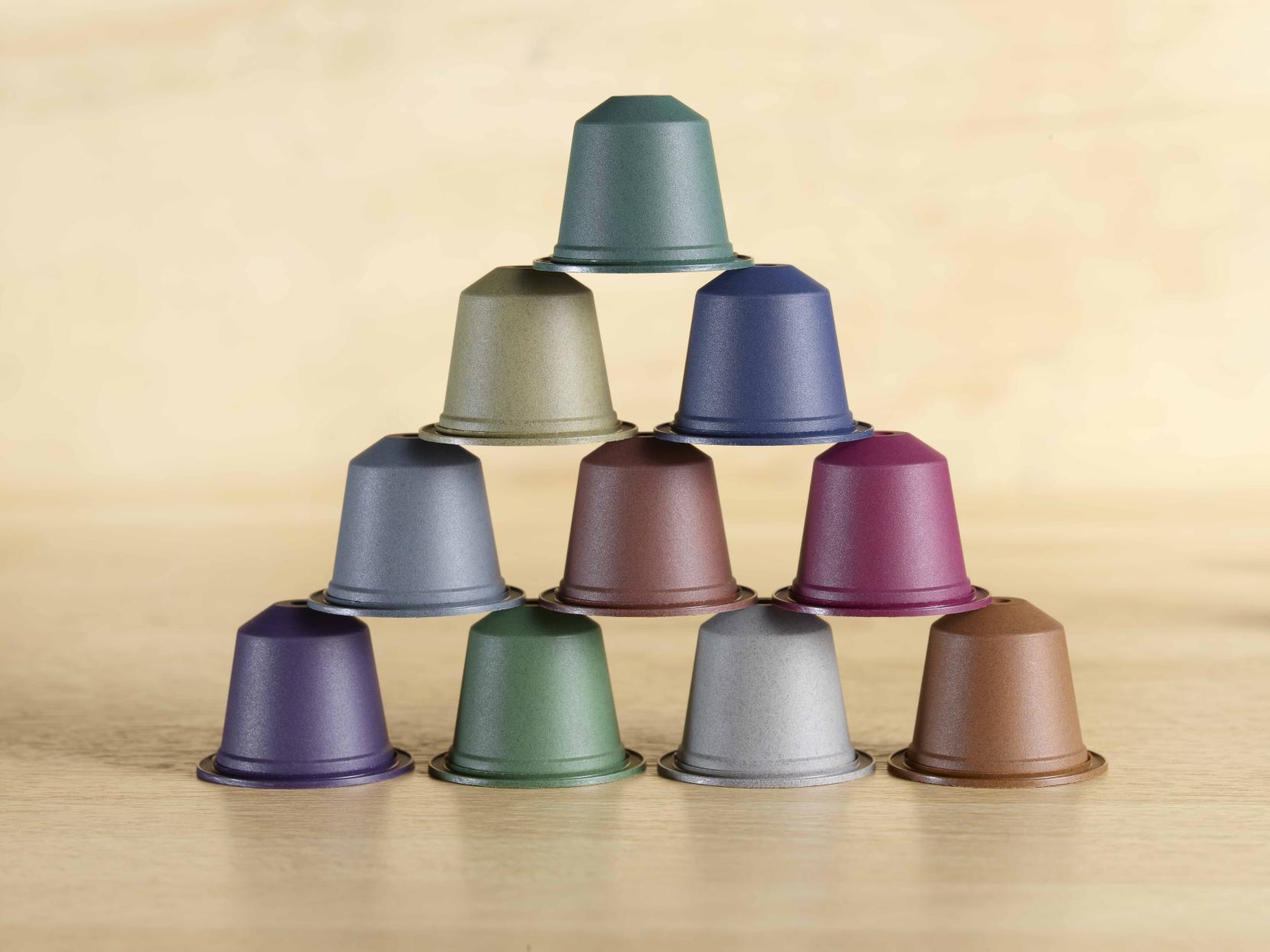 Ten home compostable coffee capsule are piled in a pyramid, showing different natural colors on a wooden background. These capsules are manufactured by Blue Circle Packaging.
