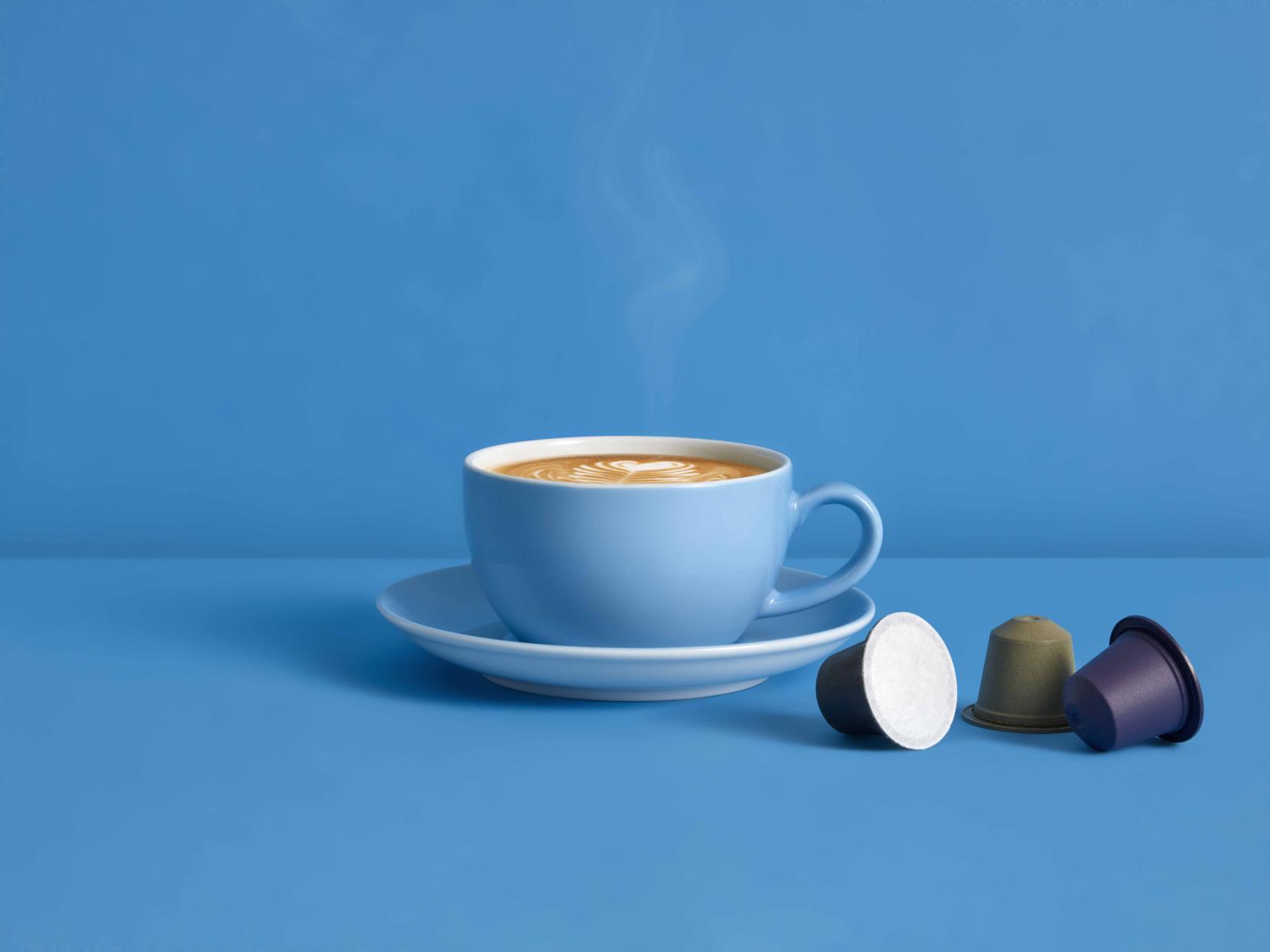 Coffee on a blue table and blue background with three single-serve Blue Circle Packaging home-compostable coffee capsules in multiple colours