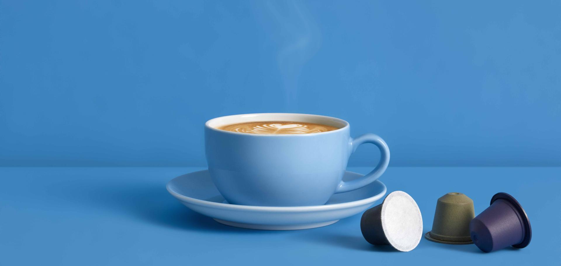Coffee on a blue table and blue background with single-serve Blue Circle Packaging home-compostable coffee capsules in multiple colours